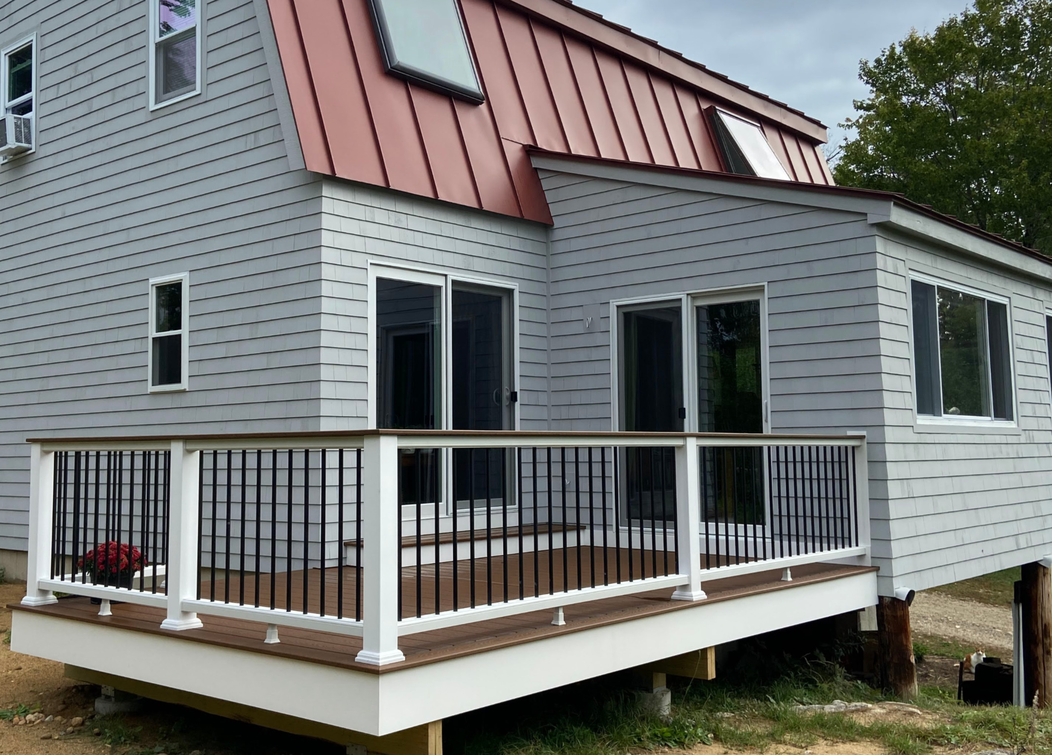 Heart + Hammer’s finished white deck with dark railings beside a gray New Hampshire home